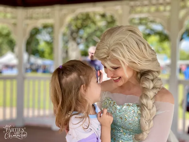 Elsa leaning down to talk with a small girl inside a park gazebo