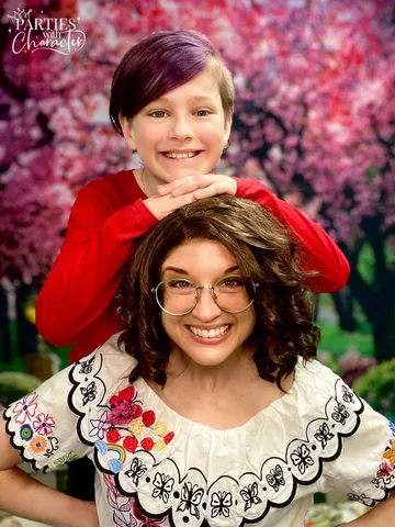 Mirabel laughing as a young boy rests his arms on top of her head