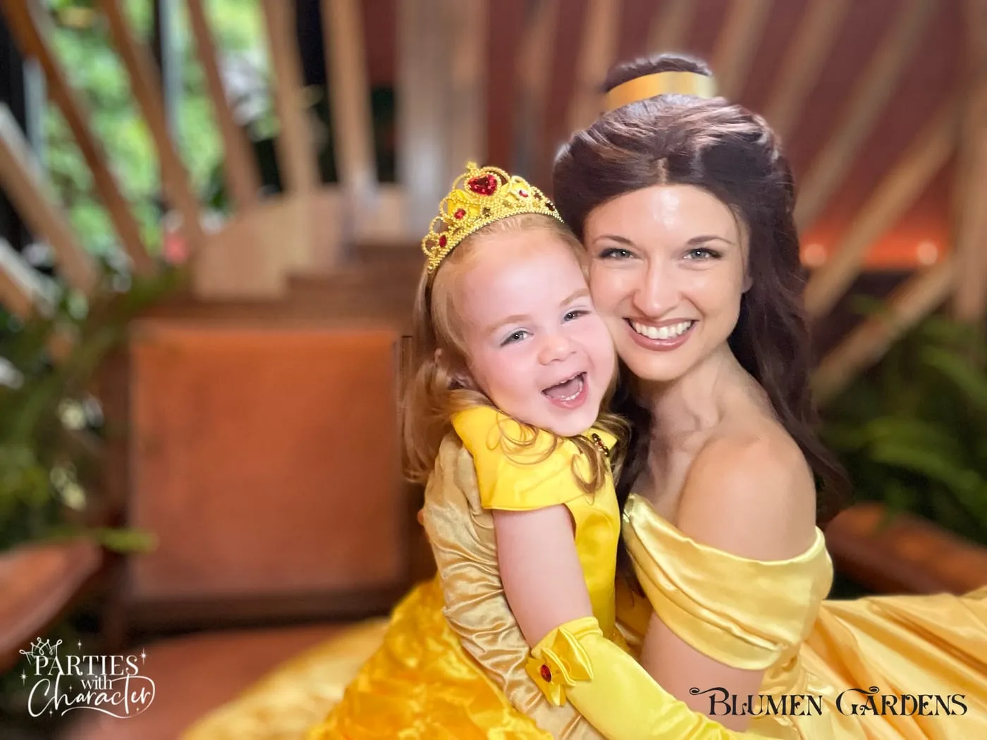 Belle laughing with a toddler in a gold crown and matching yellow dress