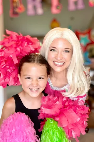 Addison holding pom-poms with a young girl at an indoor birthday party