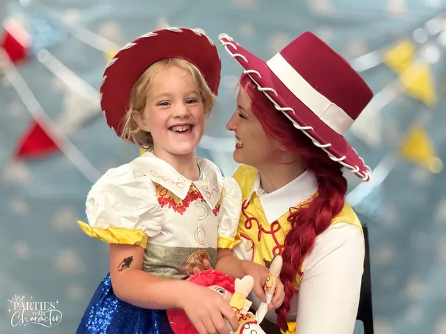 A laughing girl in a matching Jessie costume holds her Jessie doll while Jessie looks down at her