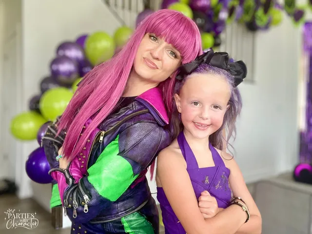 Mal hugging a young girl in front of a purple and green balloon arch