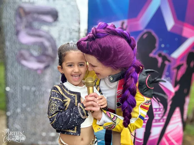 Rumi leaning forehead-to-forehead with a young girl at a birthday party