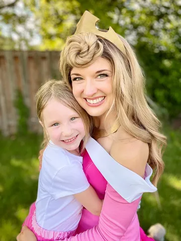 Aurora hugging a young girl in a white sash in a backyard