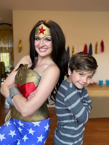 Wonder Woman and a young boy posing back to back with arms crossed like superheroes