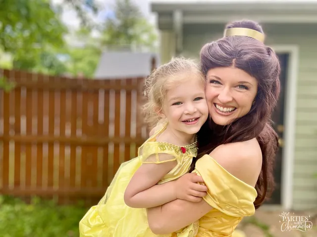 Belle embracing a laughing toddler girl in a backyard by a wooden fence