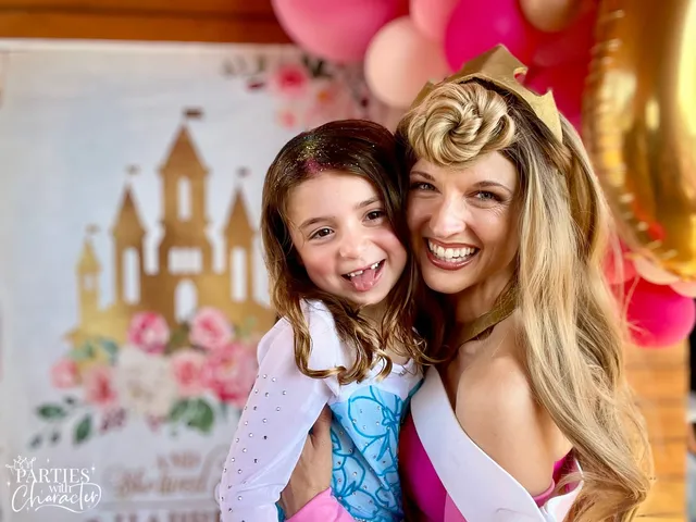 Aurora smiling with a girl in a blue dress and tiara at a party