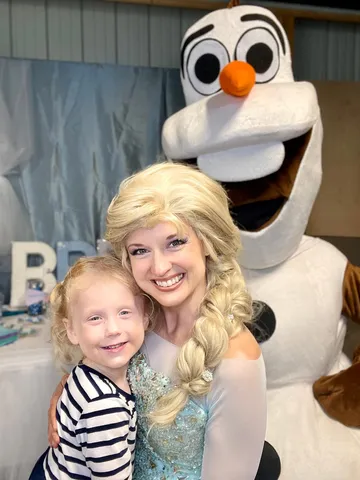 Elsa and Olaf posing with a young girl in a barn-style venue decorated for a party