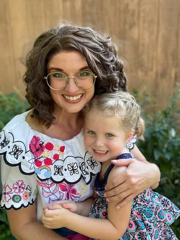 Mirabel hugging a freckled girl in front of a wooden fence