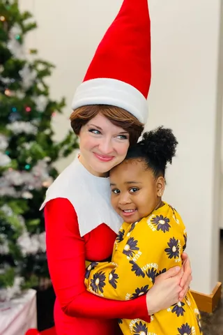 Elf on the Shelf hugging a young girl in a yellow floral dress