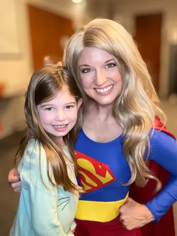 A young girl standing arm in arm with Supergirl in a library hallway