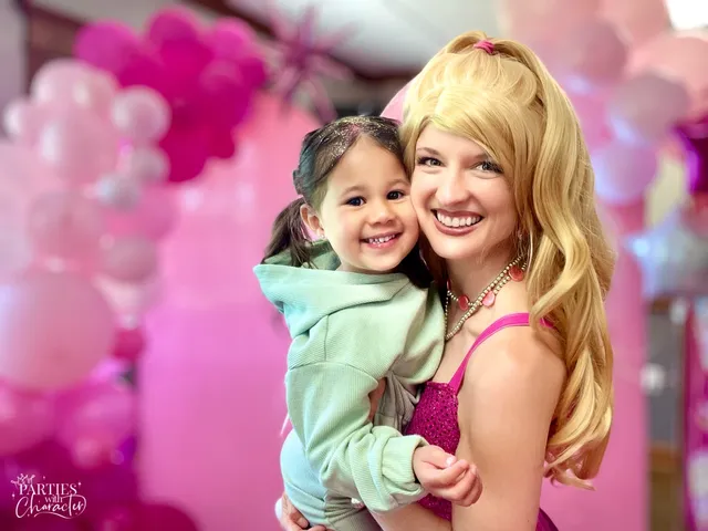 Barbie carrying a young girl in a mint hoodie past pink party balloons