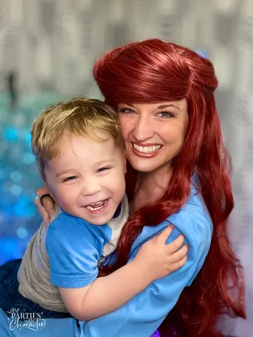 Ariel hugging a young blond boy in front of a glitter curtain