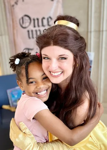 Belle hugging a young girl tightly at a library visit