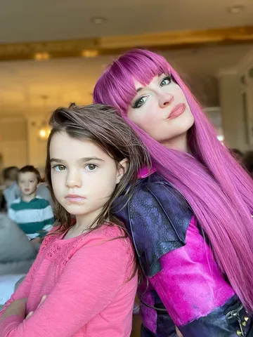 Mal with her arm around a young girl in pink at an indoor venue