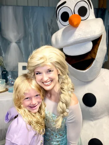 Elsa and Olaf smiling alongside a young girl in a lavender top at her party