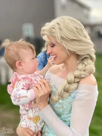 Elsa holding a baby girl who reaches up to touch her face in a backyard
