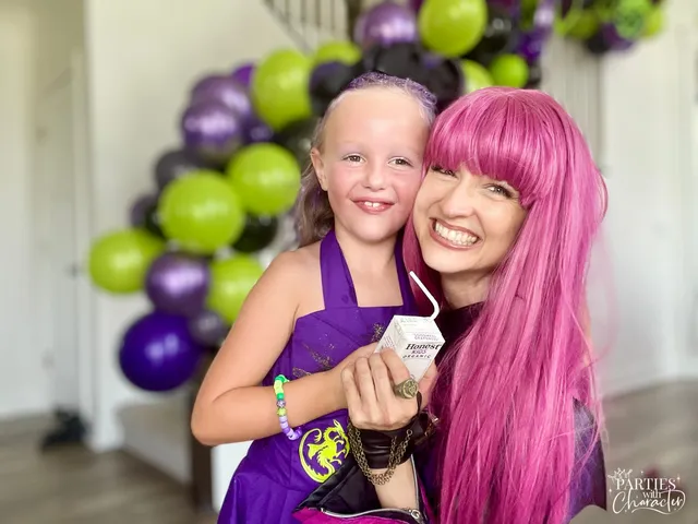 Mal laughing with a young girl holding a juice pouch beside party balloons