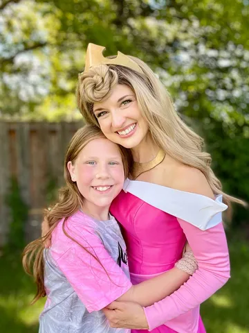 Aurora embracing a young girl in a grey cardigan outdoors