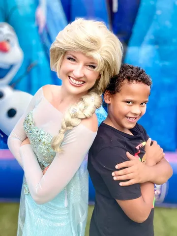 Elsa standing back to back with a boy in front of a Frozen bounce house