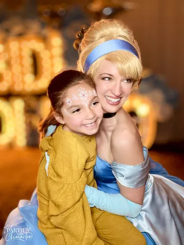 Cinderella embracing a young girl in a mustard-colored cardigan at the party