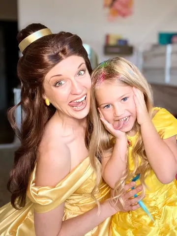 Belle and a young girl making silly squished-cheek faces together