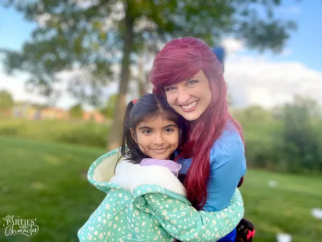 Ariel hugging a young girl in a green and white outfit outdoors