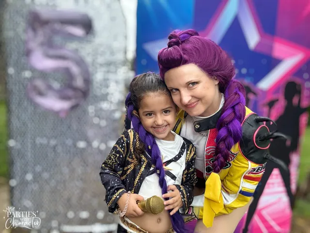 Rumi cheek to cheek with a young girl wearing matching purple braids at a birthday party