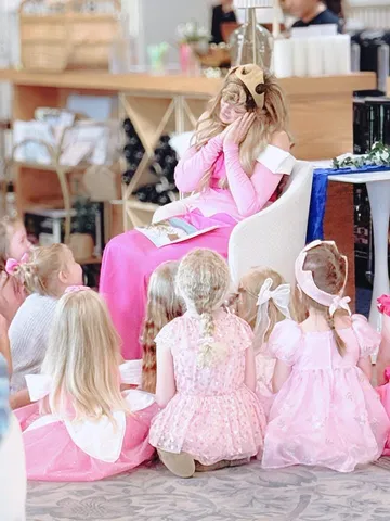 Aurora with an open storybook and a group of girls in pink dresses seated on the floor