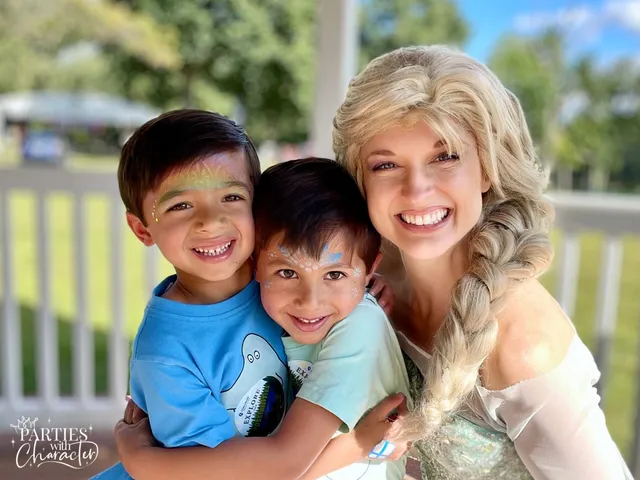 Elsa holding two young boys with snowflake face paint at a park gazebo