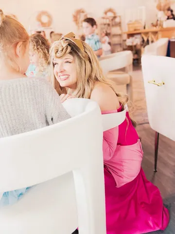 Aurora laughing as she leans on a chair back at an indoor party table