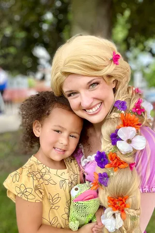 Rapunzel smiling with a young girl holding a small toy at a park