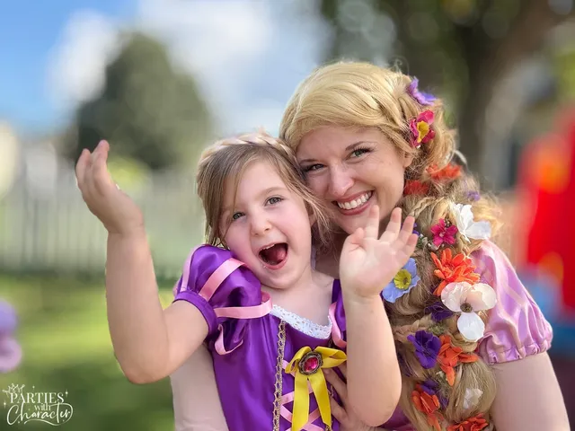 Rapunzel and a young girl in a purple Rapunzel dress cheering with hands raised at a backyard party