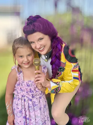 Rumi arm in arm with a girl in a lavender dress holding a microphone