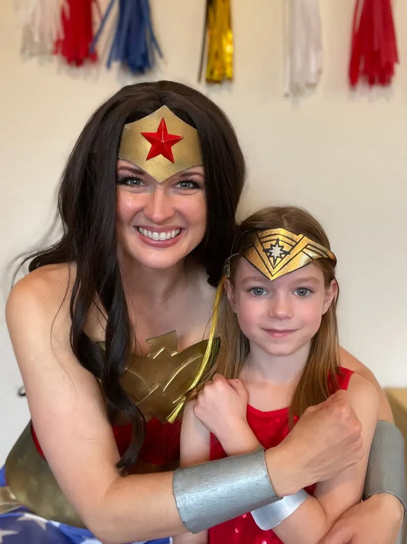 Wonder Woman embracing a young girl wearing a paper tiara headband at her party