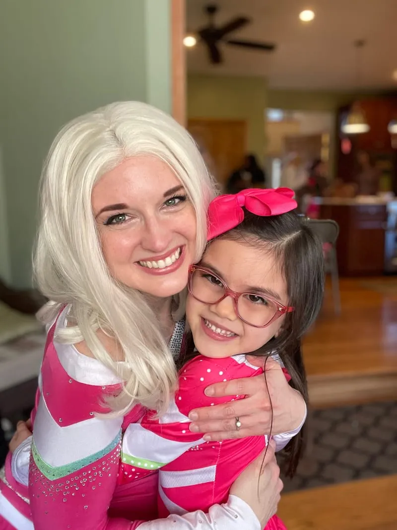 Addison hugging a smiling young girl wearing glasses at a birthday party