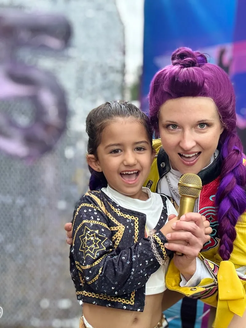 Rumi beaming with a delighted young girl at an outdoor birthday party