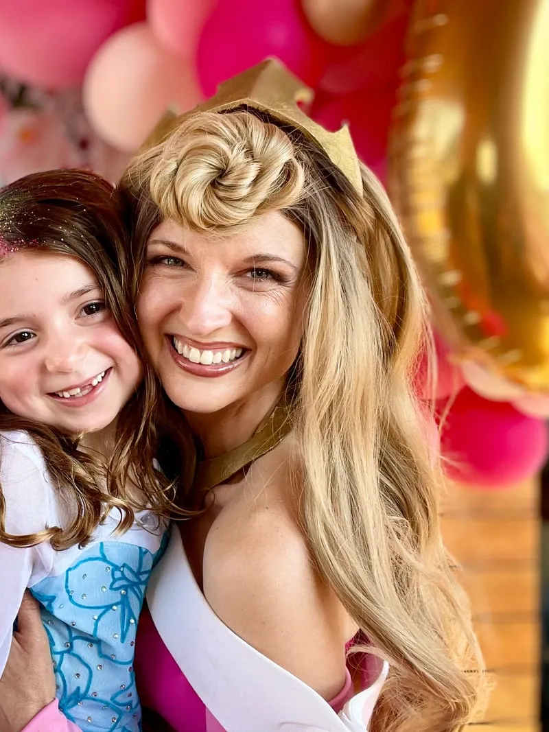 Aurora and a girl in a tiara smiling together at a castle-themed party