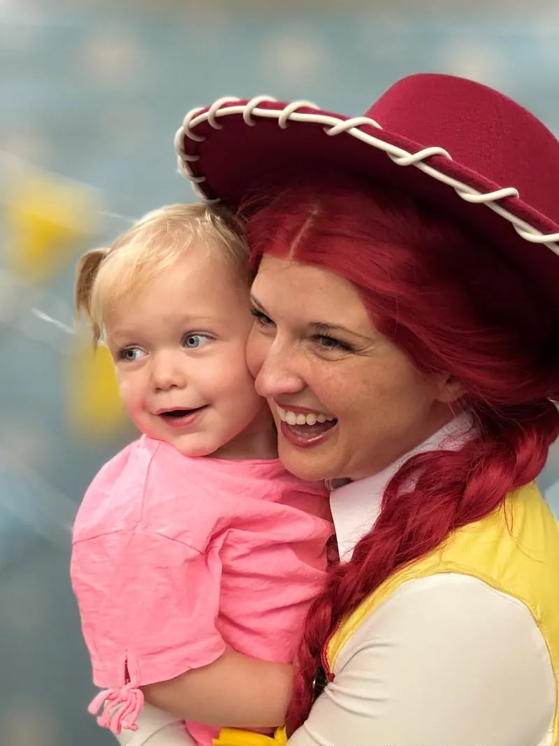Jessie from Toy Story cheek-to-cheek with a delighted toddler in a pink shirt