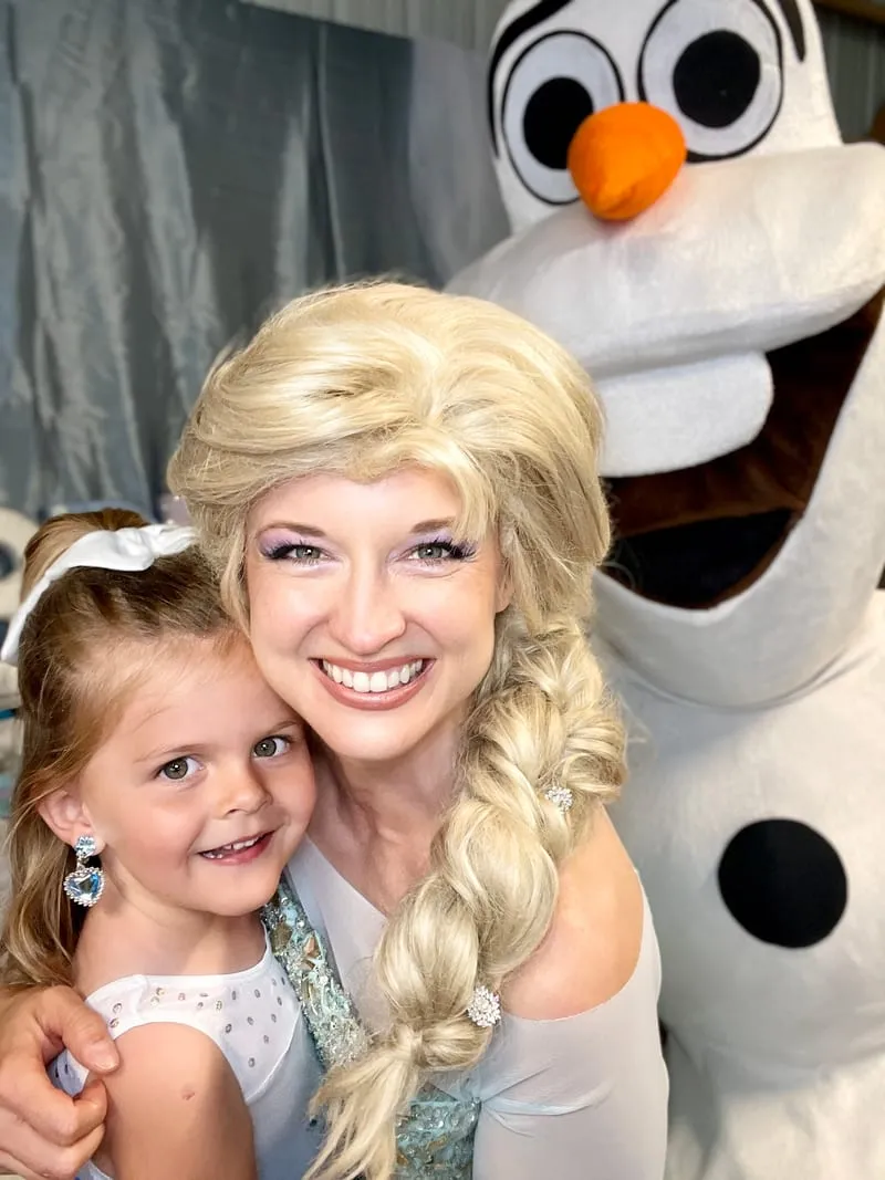 Elsa and Olaf posing with a young girl wearing a sparkly bow at her party