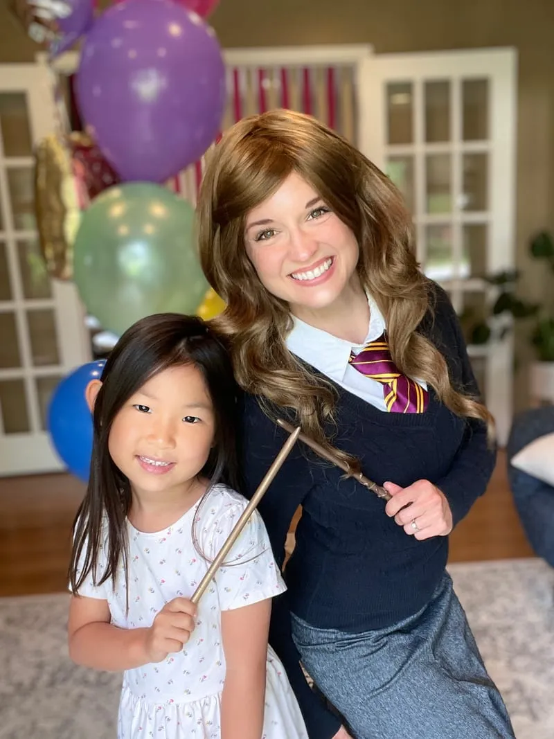 Hermione Granger standing close to a young girl holding a wand at a birthday party