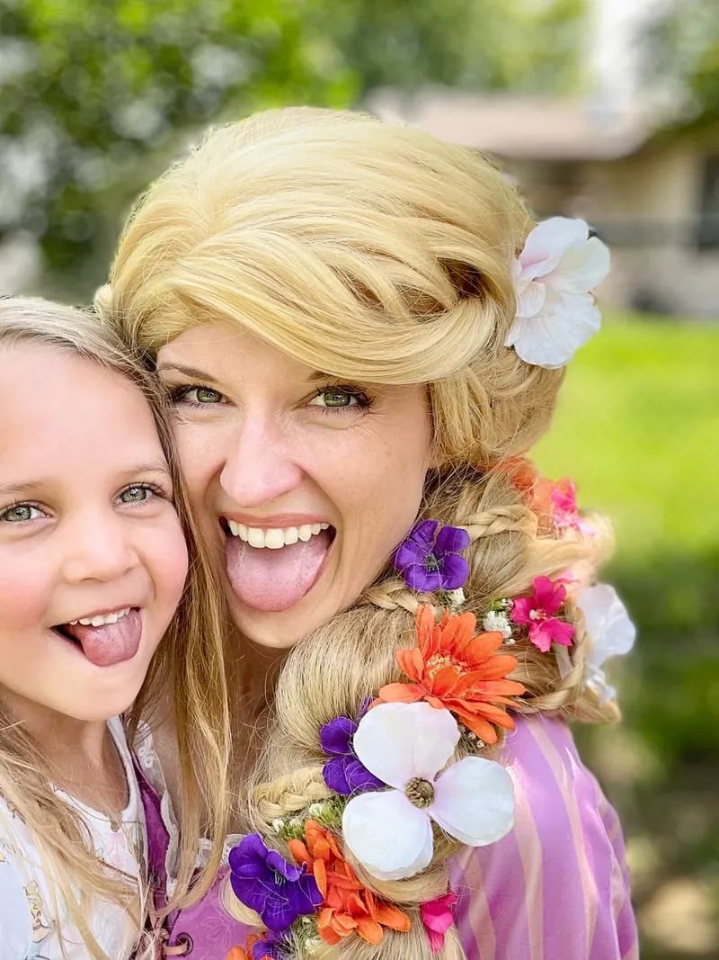 Rapunzel and a young girl laughing cheek to cheek outdoors
