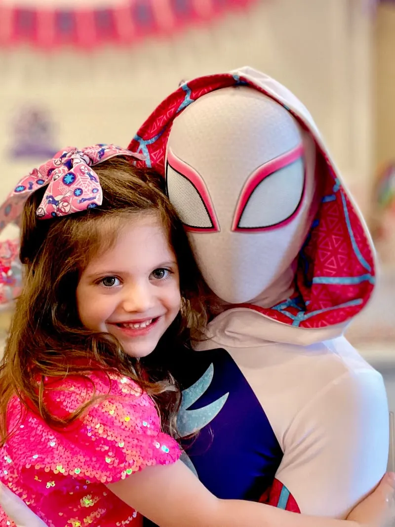 Ghost Spider hugging a young girl wearing a hair bow at a party