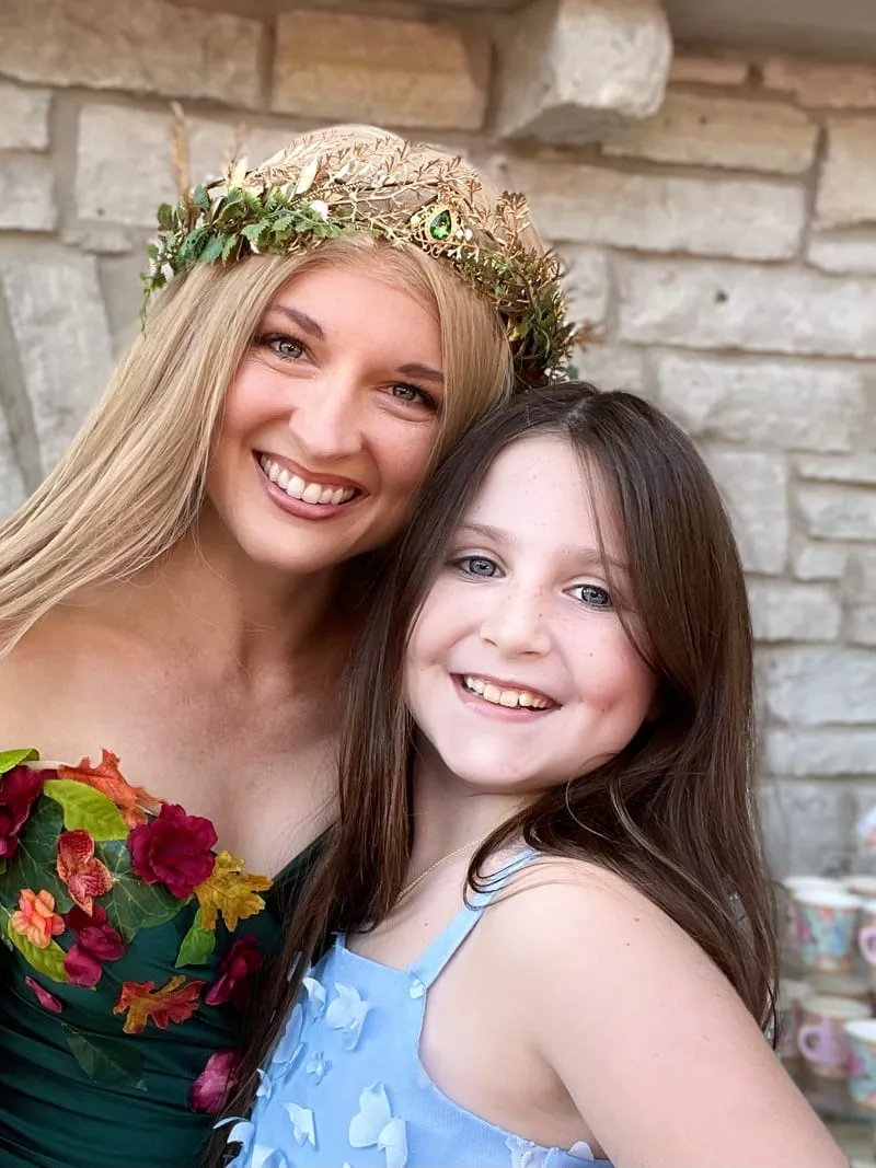 Woodland Fairy embracing a smiling young girl in a butterfly-print dress