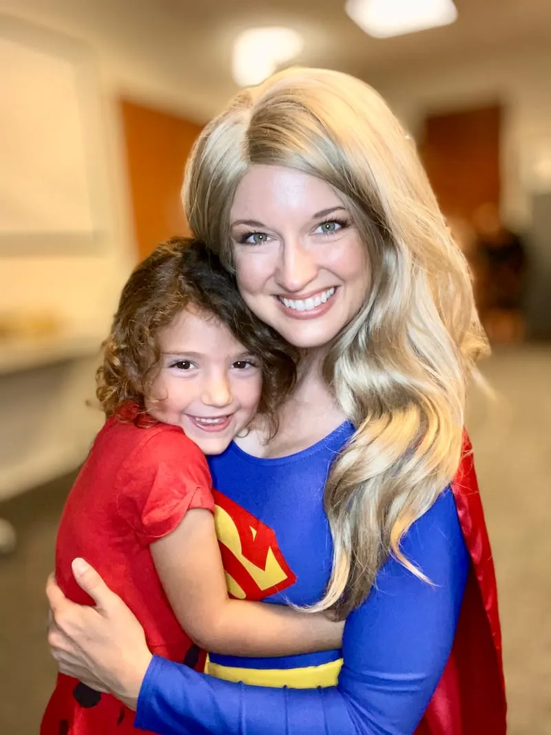Supergirl hugging a young child dressed in a red superhero costume