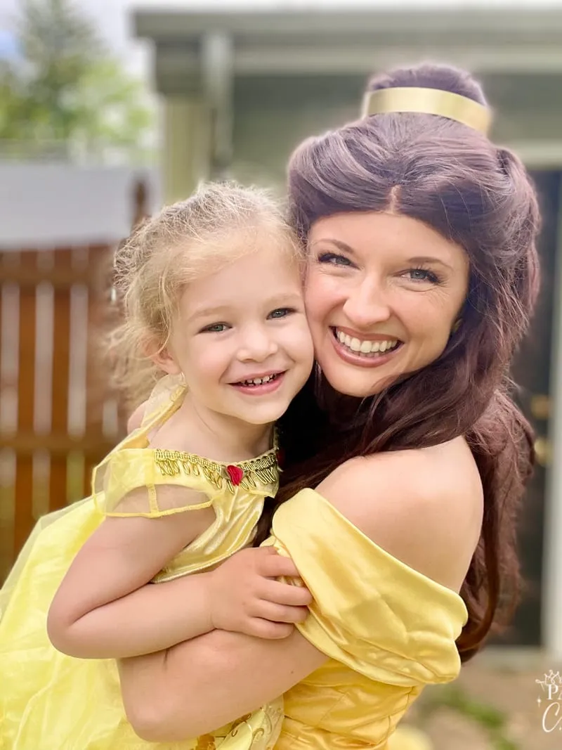 Belle cheek to cheek with a laughing toddler girl in a matching yellow dress