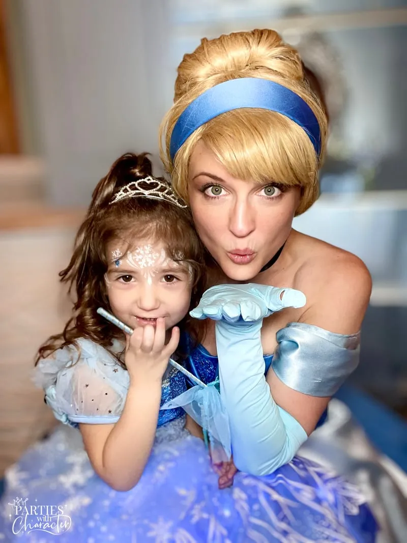 Cinderella and a young girl blowing a kiss together while holding a sparkly wand